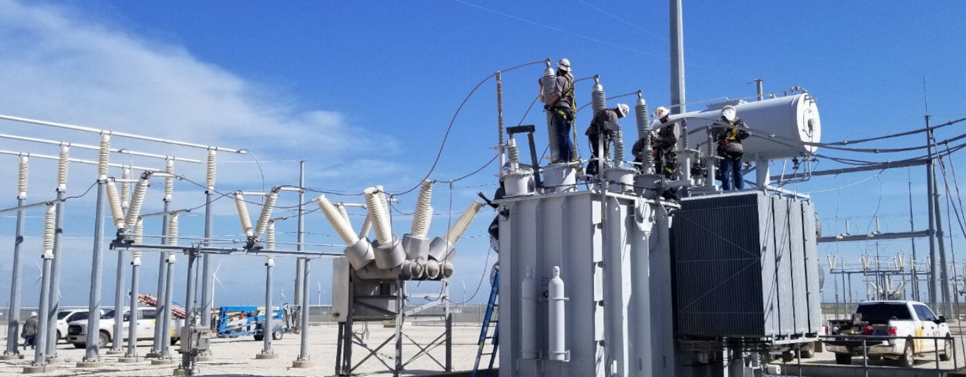 4 workers on the top of an industrial sized transformer